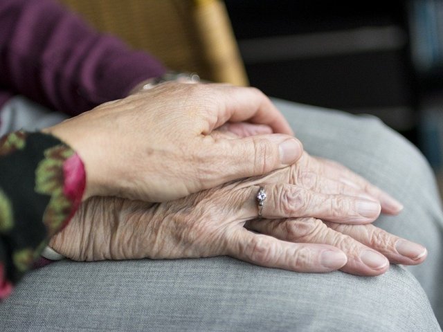 jedna, młodsza kobieca dłoń leży na dłoni pomarszczonej, starszej. Gest wsparcia