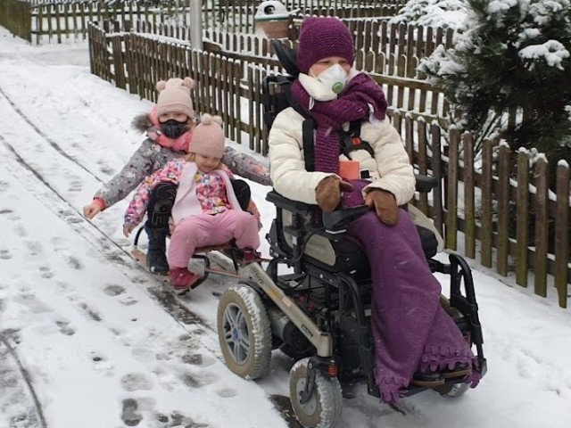 Fotografia mamy z SMA z dwiema córkami w zimie na sankach.