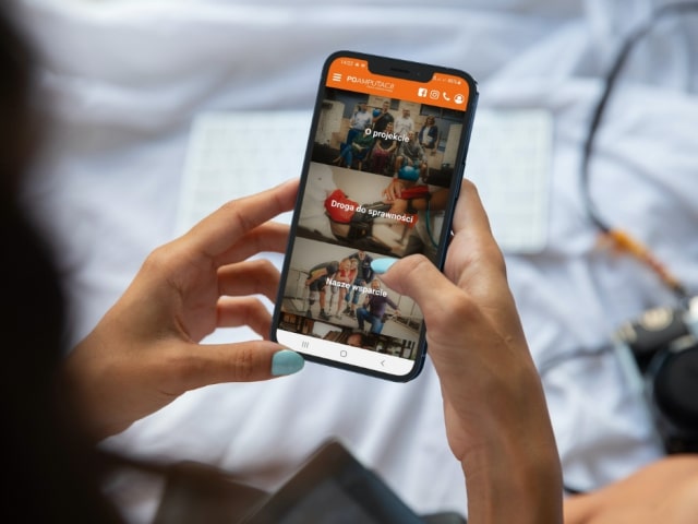 Fotografia na której widnieje osoba trzymająca telefon i używająca aplikację "Po amputacji".