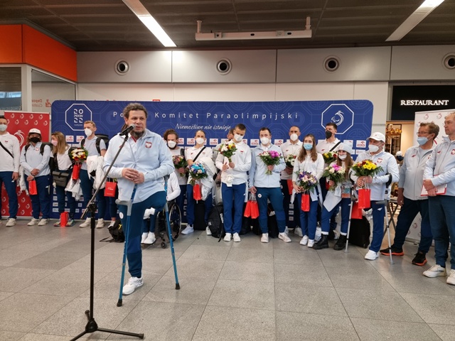 Łukasz Szeliga, szef Polskiego Komitetu Paraolimpijskiego, wypowiada się do mikrofonu. Za nim reprezentacja Polski