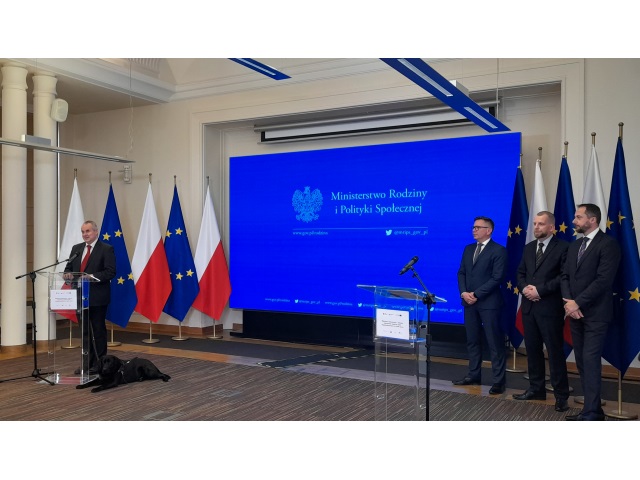 W sali konferencyjnej Ministerstwa Rodziny i Polityki Społecznej trfa briefing. Przy mównicy stoi Pełnomocnik Rzadu ds. Osób Niepełnosprawnych Paweł Wdówik. Po prawej stronie sali stoją Krzysztof Kotyniewicz z PZG, Krzysztof Kosiński z POPON i Krzysztof Siewiera ze Stowarzyszenia Czas Przestrzeń Tożsamość. Po środku jest duży ekran, na którym wyświetla się nazwa Ministerstwa.