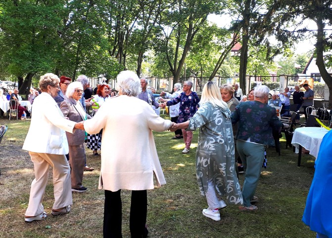 Potańcówka seniorów. Starsze osoby tańczące w kółku, uśmiechają się. 