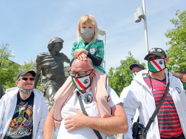 kilku kibiców stowarzyszenia w maskach na ramionach jednego z nich siedzi dziewczynka