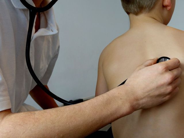 lekarz ze słuchawkami bada chłopca, przykładając mu stetoskop na plecy