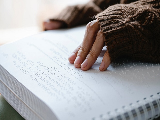 Na obrazku jest przedstawiona dłoń dotykająca książki napisanej w języku Braille