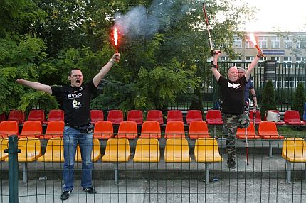 Dwóch niepełnosprawnych kibiców na trybunach trzyma zapalone race