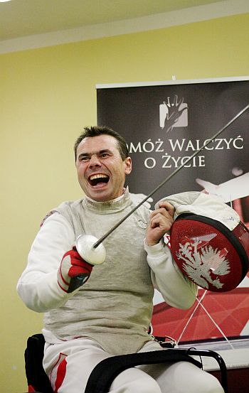 Jacek Gaworski w stroju szermierczym, za nim tablica z napiszem: 
