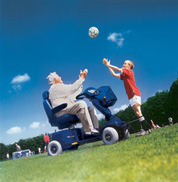 zdjęcie: osoba na wózku elektrycznym łapie piłkę podczas zabawy z dzieckiem