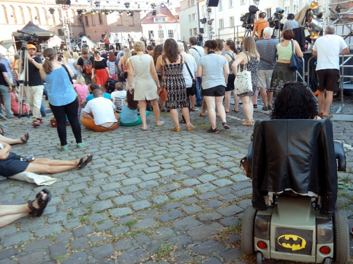 kobieta na wózku elektrycznym z naklejką Batmana w tłumie osób na koncercie
